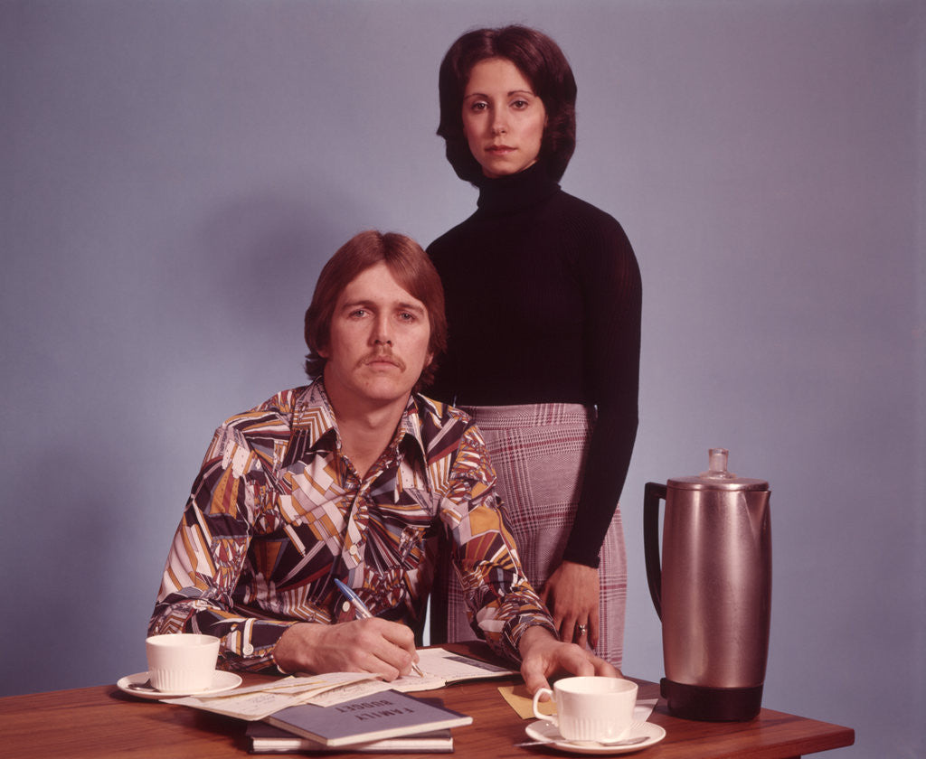 Detail of 1970s Husband Wearing Loud Print Shirt Writing Family Budget and Wife Standing Behind Coffee Pot by Anonymous