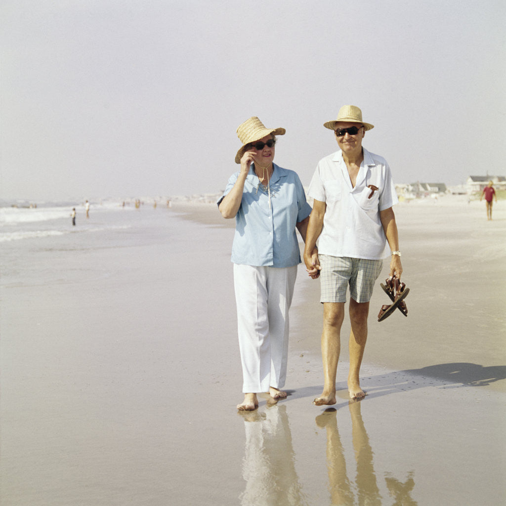 Detail of 1970s Senior Couple Walking Beach Holding Hands Wearing Straw Hats by Anonymous