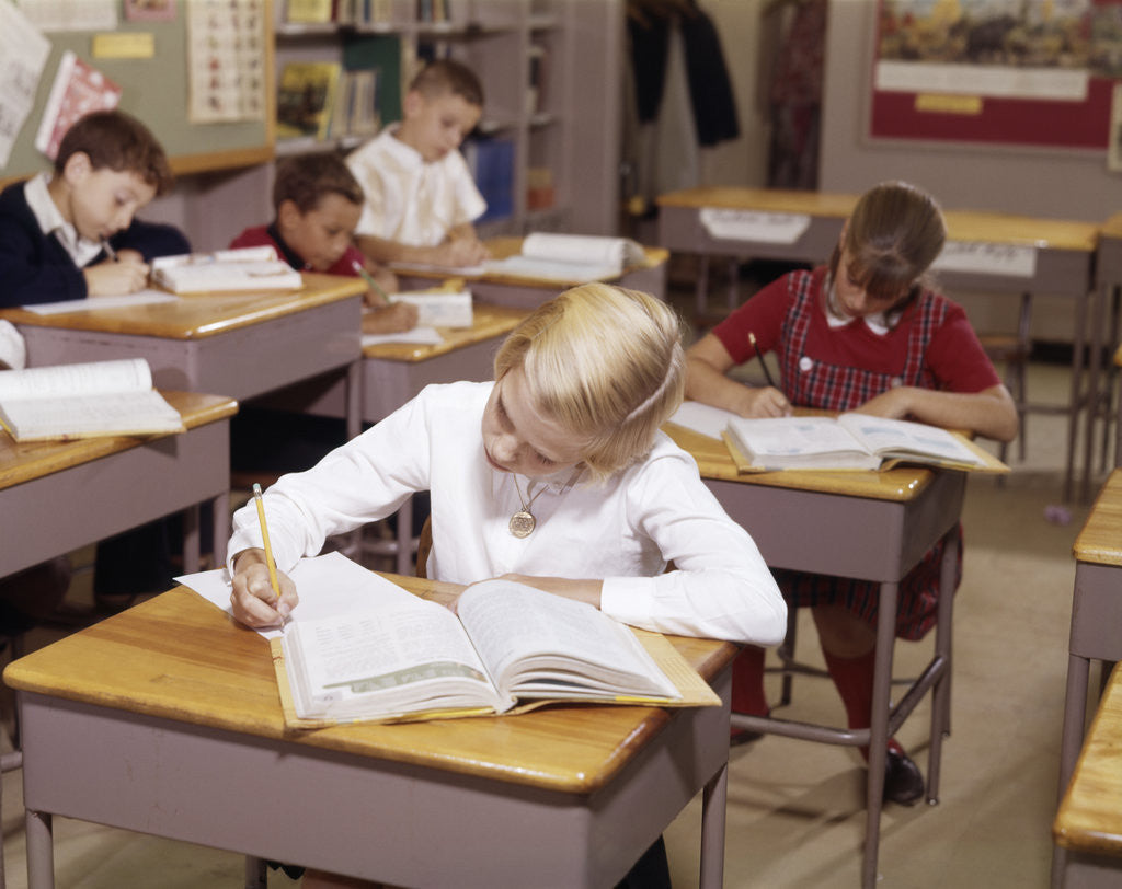 Detail of 1960s Elementary School Children In Classroom At Desks Working With Books And Papers Boy Girl by Corbis