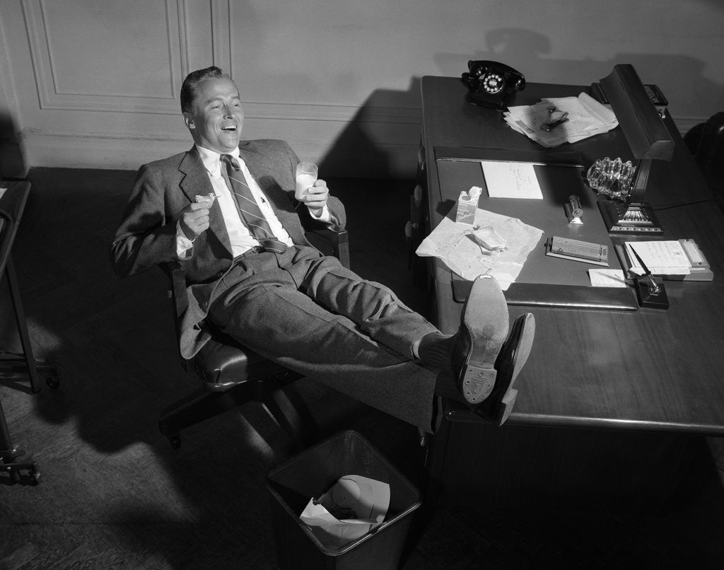 Detail of 1950s Man Businessman Salesman Eating Lunch In Office With Feet Resting Up On Desk by Corbis