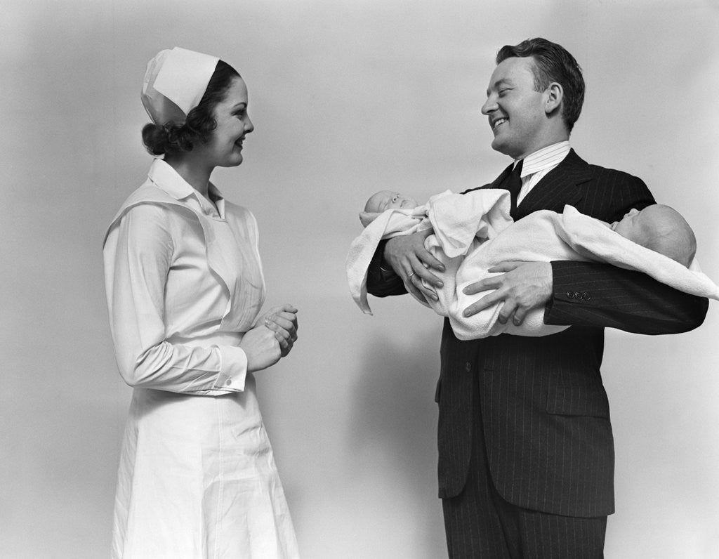 Detail of 1930s 1940s Woman Nurse Talking With Man Proud New Father Holding Newborn Twin Babies by Corbis