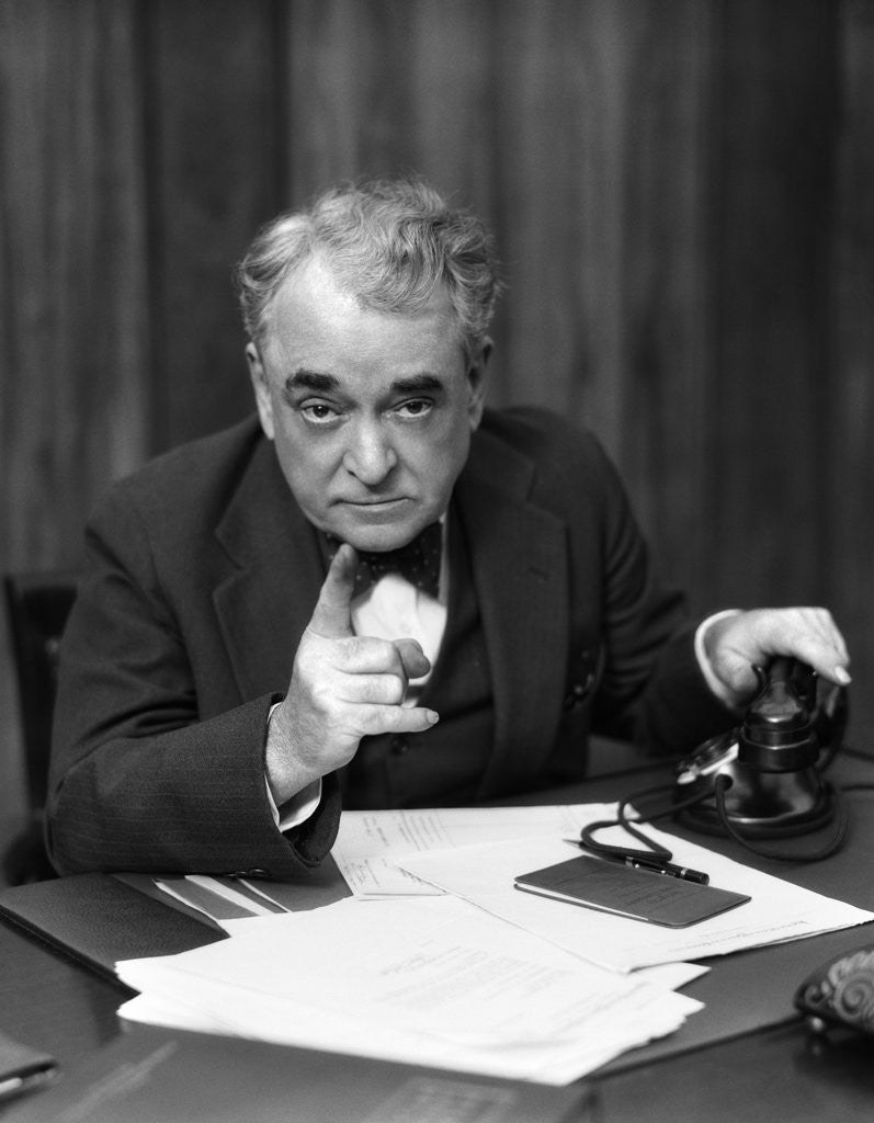 Detail of 1930s Head-On Serious Senior Businessman Behind Desk Hand On Telephone Pointing by Anonymous