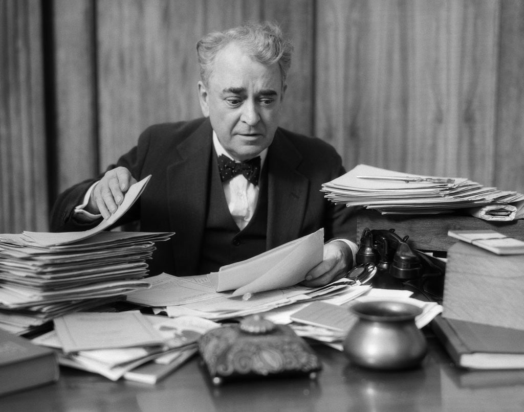 Detail of 1920s 1930s Elderly Executive Man Sitting At Desk Looking Through Papers by Corbis