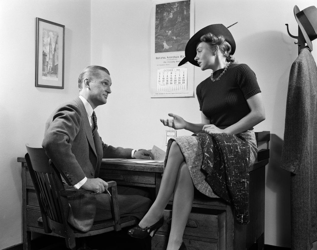 Detail of 1940s Woman Sitting On Desk Hat Skirt Hand Gesture Talking Flirting With Man by Anonymous