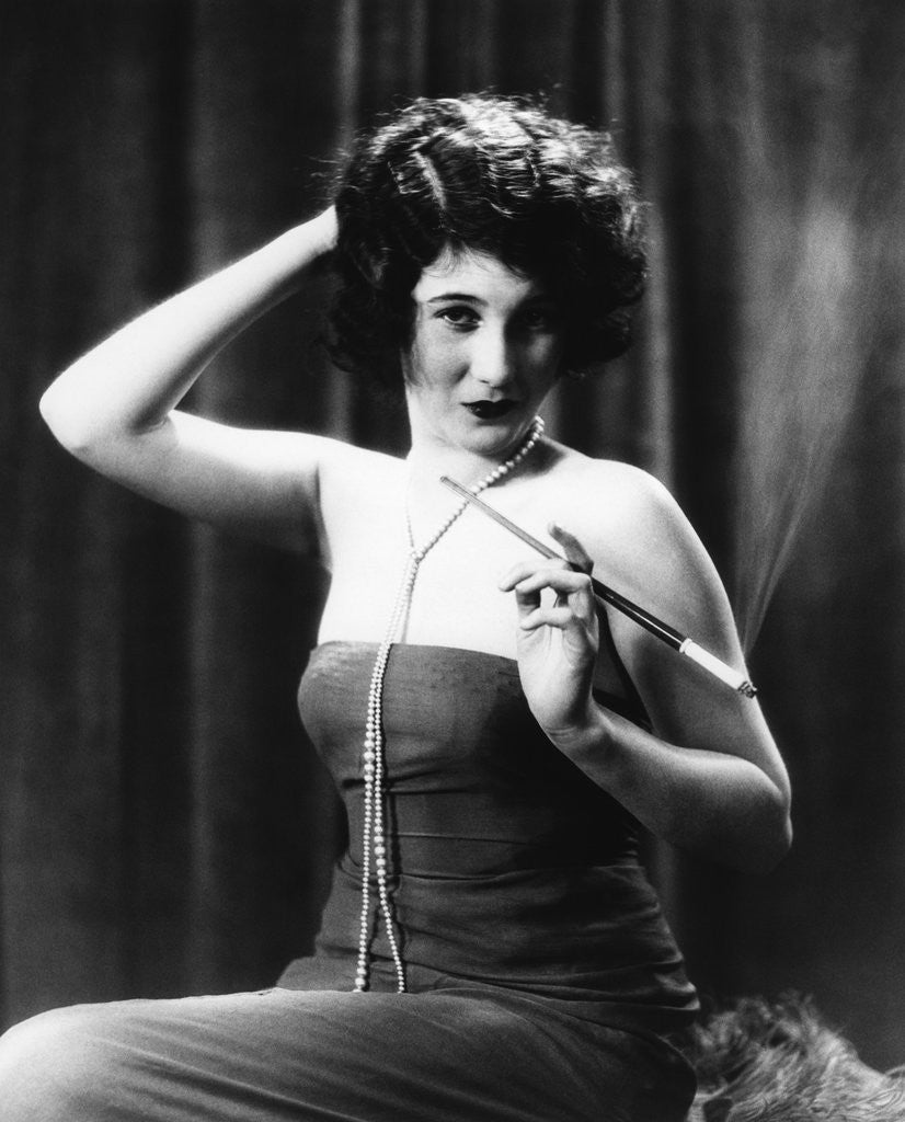 Detail of 1920s Woman Wearing Strapless Gown String Pearls Holding Cigarette Holder Hand On Back Of Head by Corbis