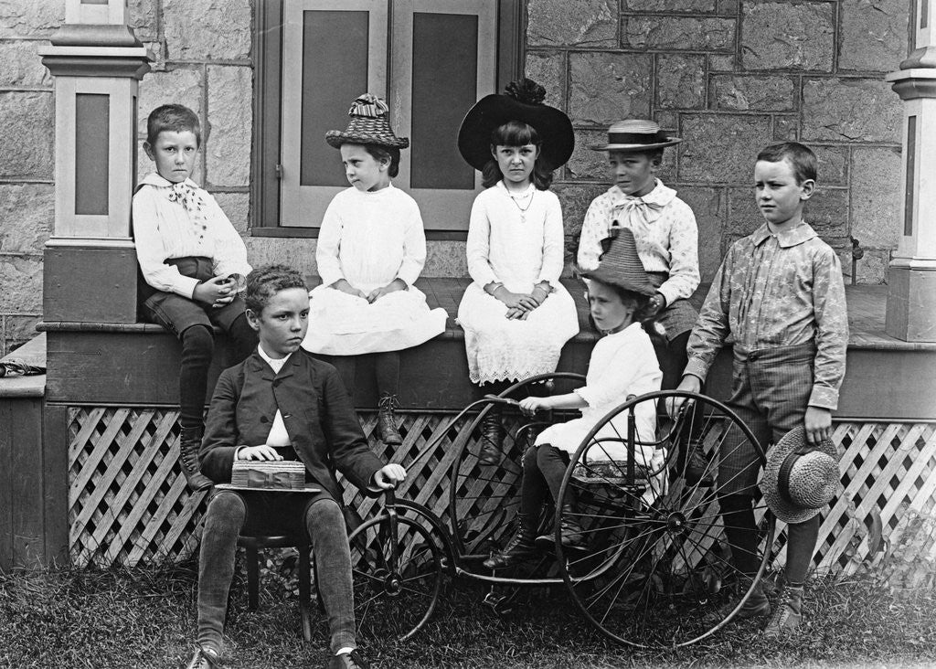 Detail of 1890s 1900s Seven Children Sitting On and Around Porch One Girl On Old Fashioned Tricycle by Corbis