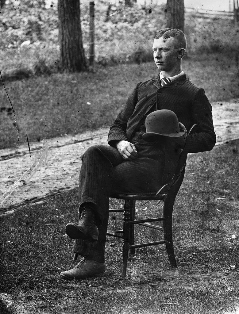 Detail of 1890s 1900s Side View Of Man Wearing Suit Seated On Chair Outside Holding Bowler Hat by Anonymous