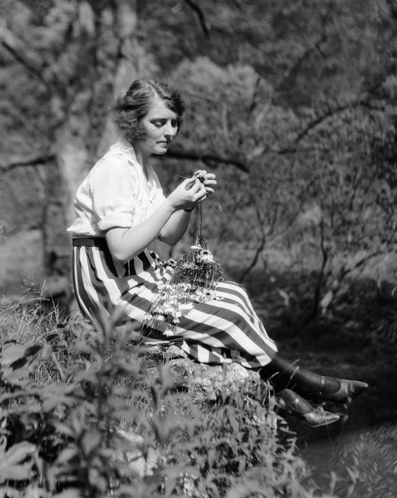 Detail of 1920s Young Woman In Striped Skirt Sitting On Stream Bank In Woods Braiding Garland Of Wild Flowers by Anonymous