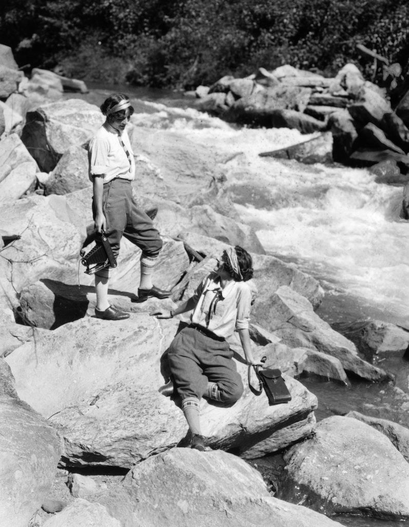 Detail of 1920s Two Women Sisters On Rocks By Creek Talking Holding Folding Camera by Corbis