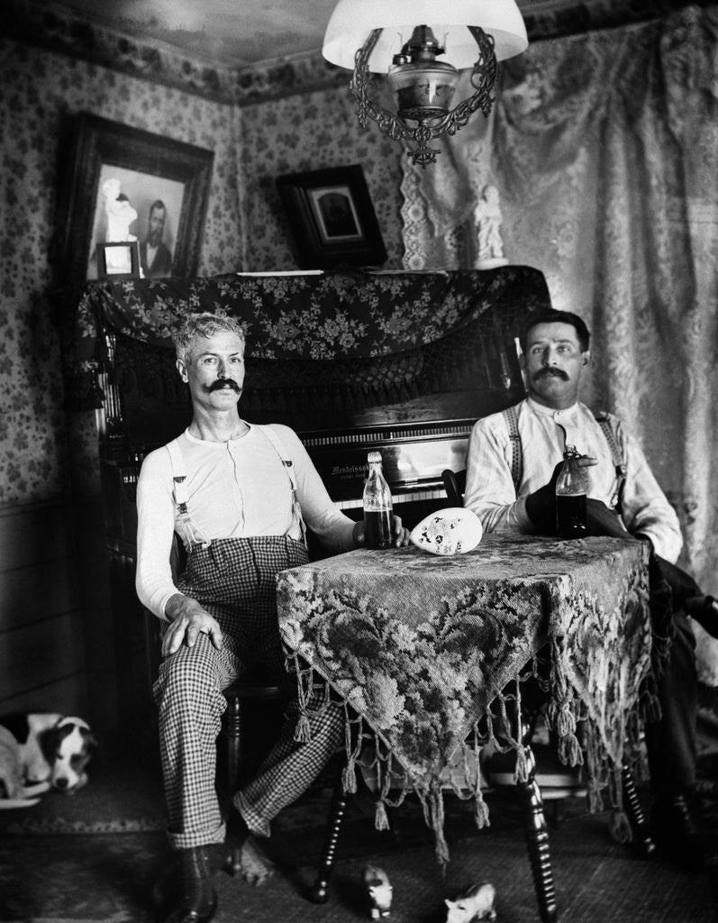 1890s Two Men In Shirt Sleeves Sitting At Table Drinking Bottles Of Beer With Piano And Dog by Corbis