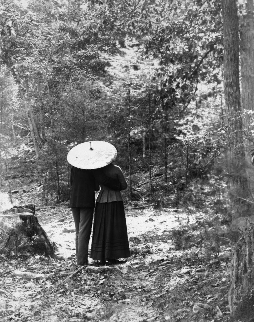 Detail of 1900 View Of Back Of Couple Walking Through Woods Under Umbrella Man With Arm Around Woman by Anonymous