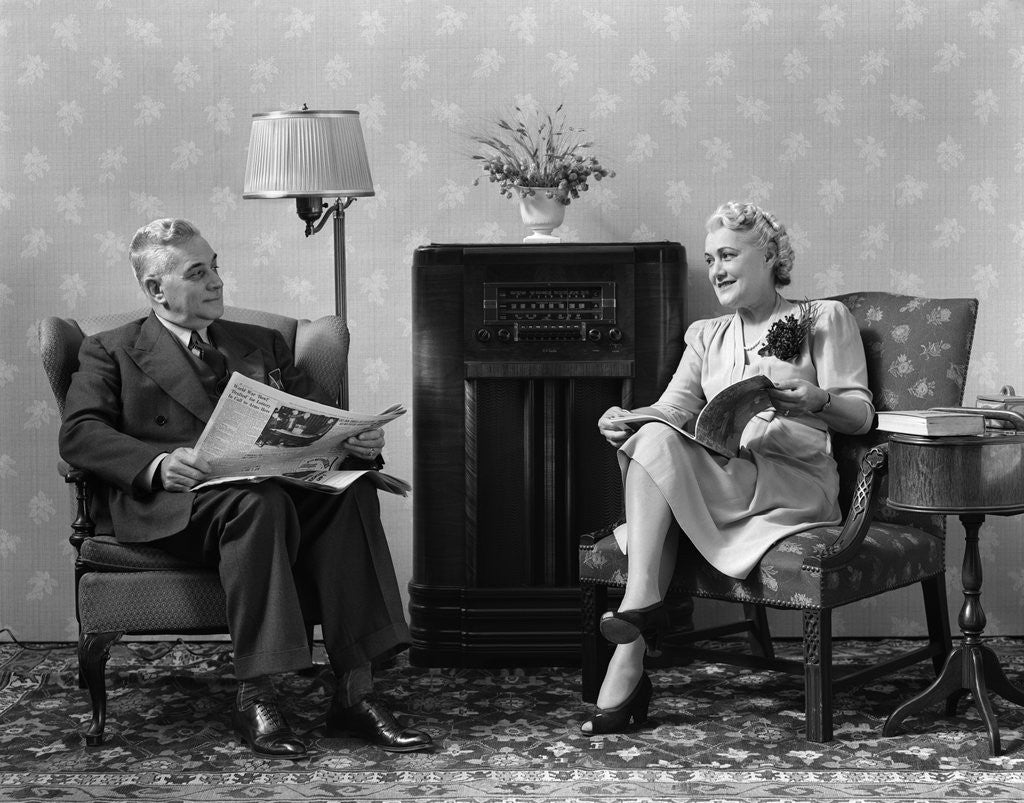 Detail of 1940s Senior Couple Sitting In Living Room Reading Newspaper And Magazine Listening To Radio by Anonymous