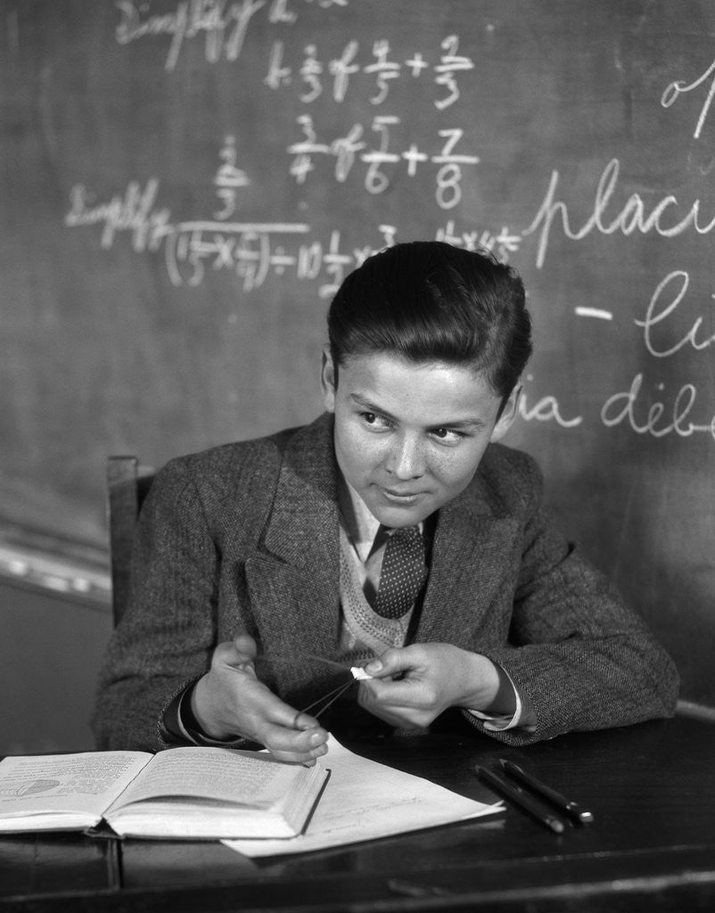 Detail of 1920s 1930s Boy At Desk In Classroom In Front Of Blackboard Shooting Paper Wad With Rubber Band by Anonymous