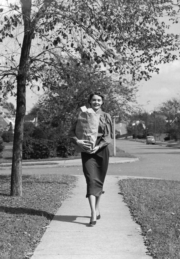 Detail of 1950s Woman Walking On Sidewalk Carrying A Grocery Bag Full Of Food by Anonymous