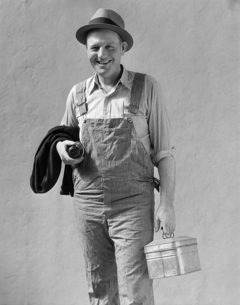 Detail of 1930s Man In Work Clothes Overalls Holding Lunch Box Thermos Bottle And Sweater by Anonymous
