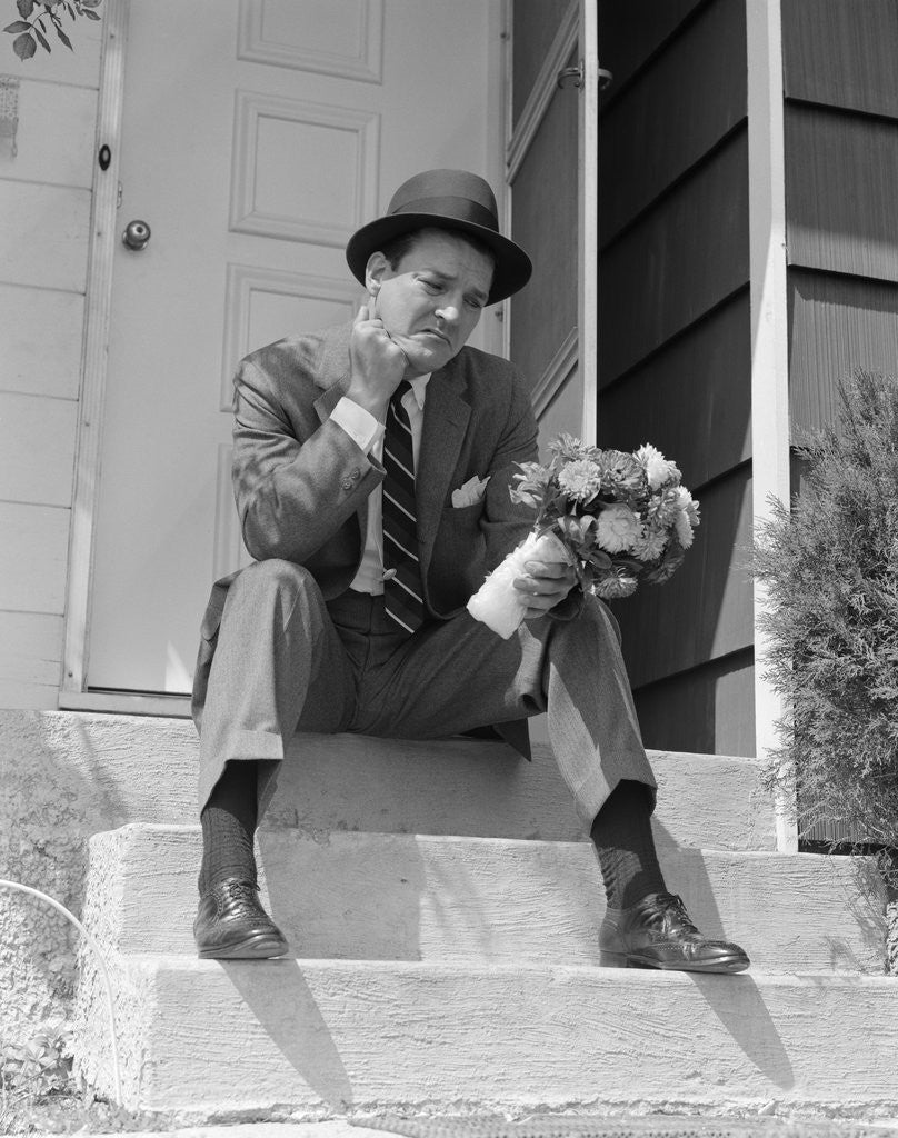 Detail of 1950s Man In Suit And Hat Holding Flowers Sitting Outside Front Door On Steps Looking Sad by Anonymous