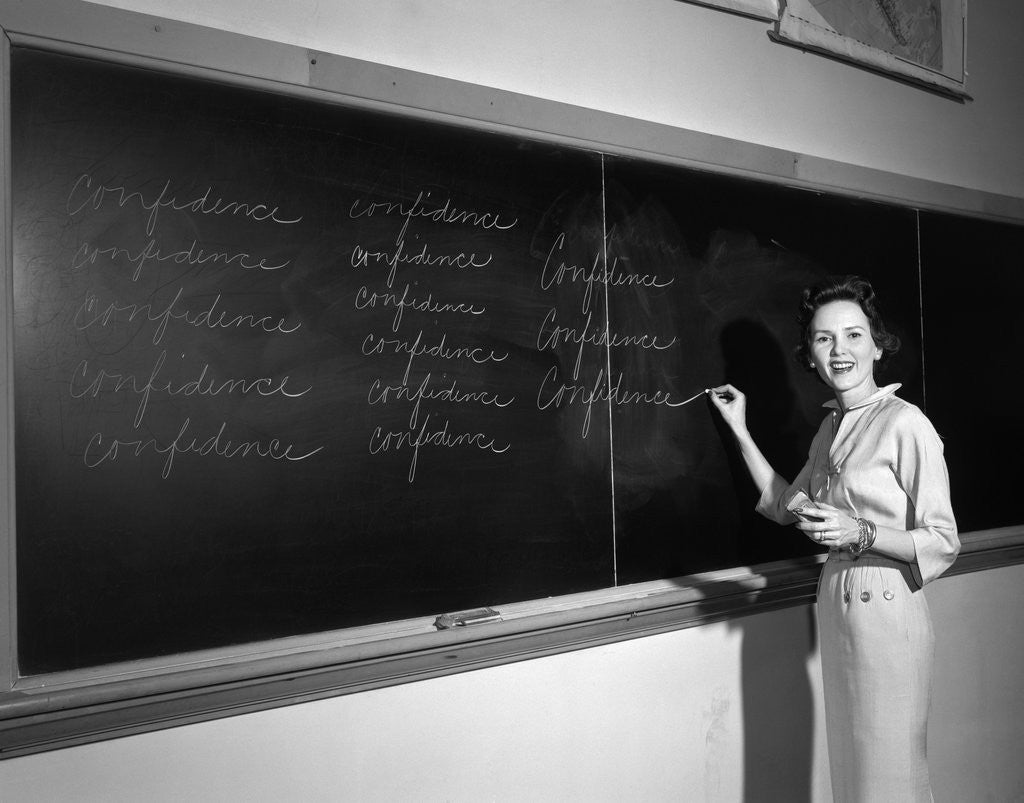 Detail of 1950s Teacher In Front Of Classroom Writing Confidence On Blackboard by Corbis
