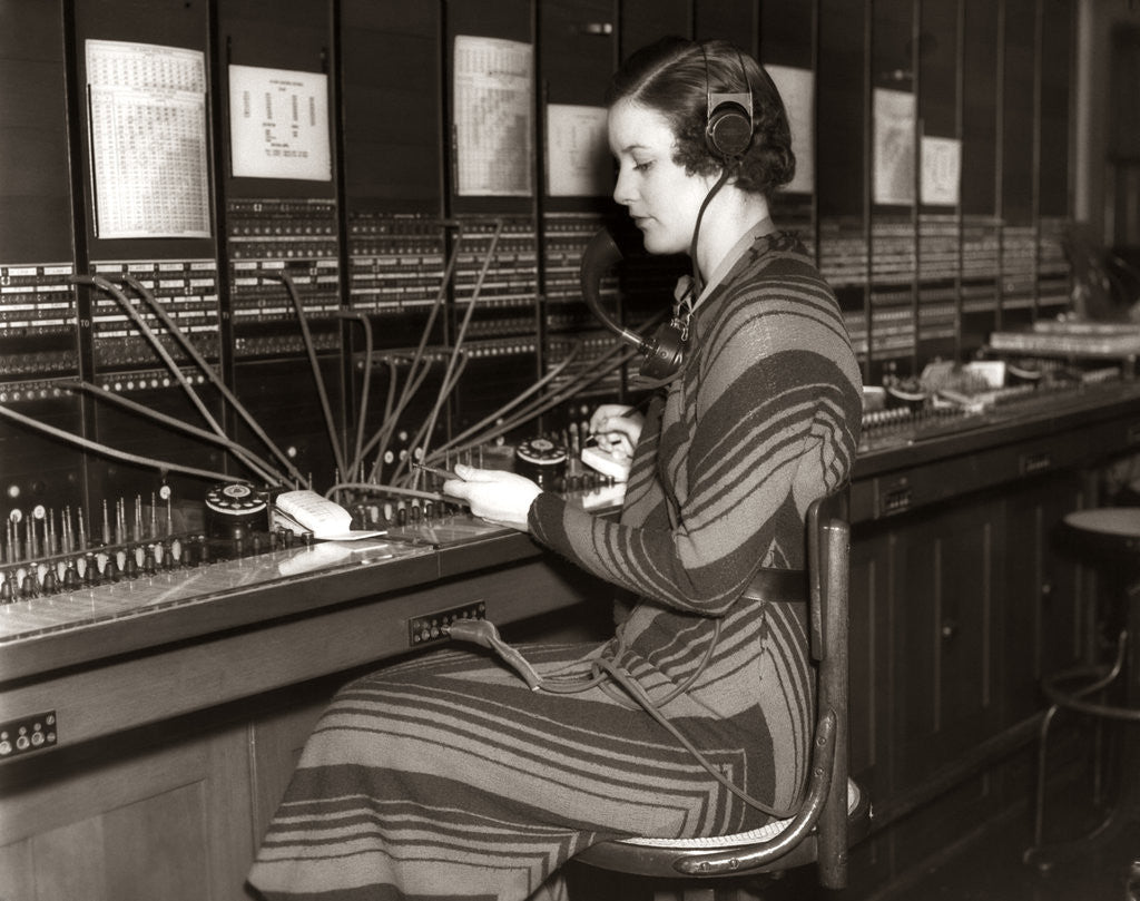 Detail of 1930s Woman Telephone Operator Sitting At Large Manual Switchboard Directing Calls by Corbis