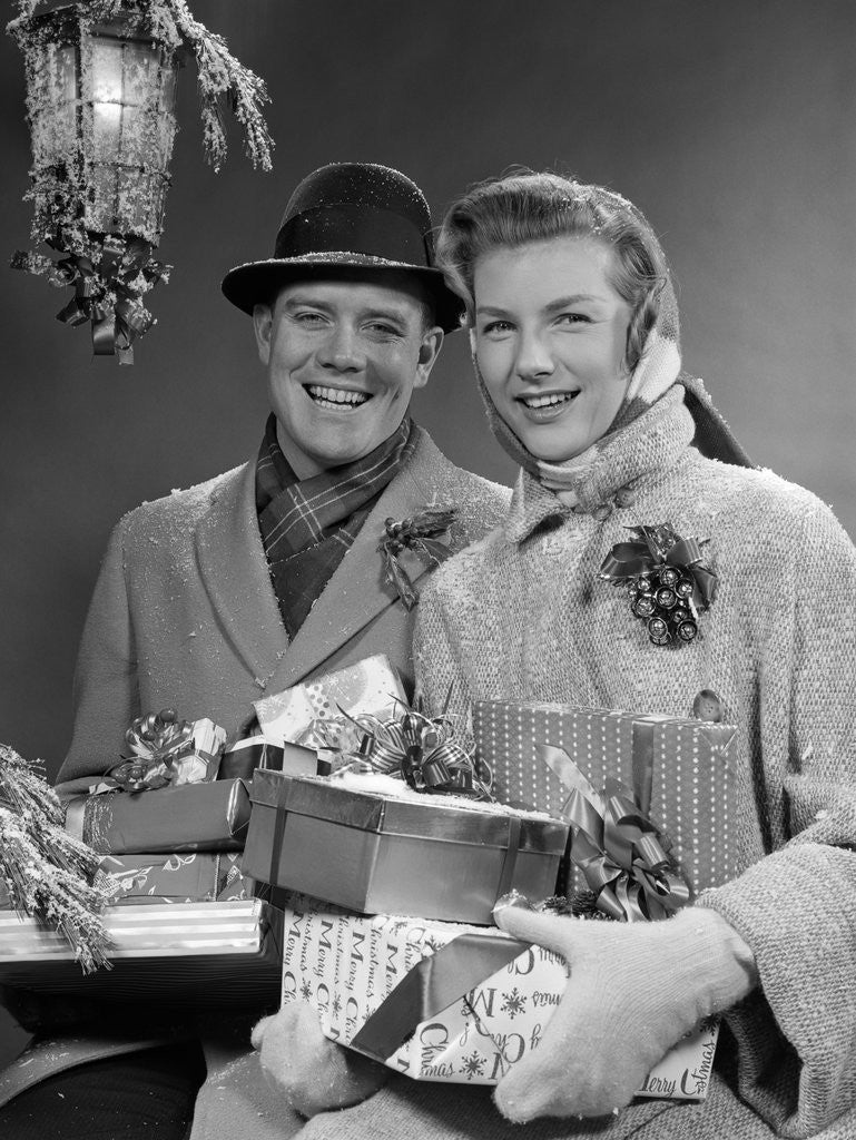 Detail of 1950s Husband And Wife Carrying Armload Of Christmas Packages Standing In Snow Under Porch Light by Anonymous