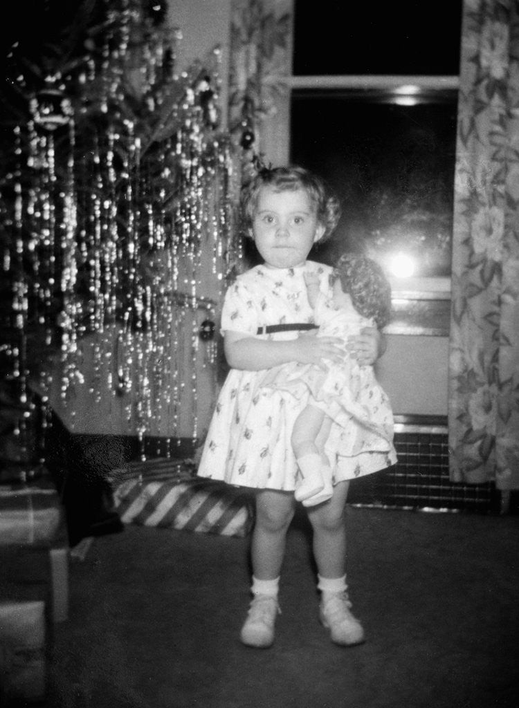 Detail of A little girl stands by the Christmas tree clutching her doll, ca. 1955 by Anonymous