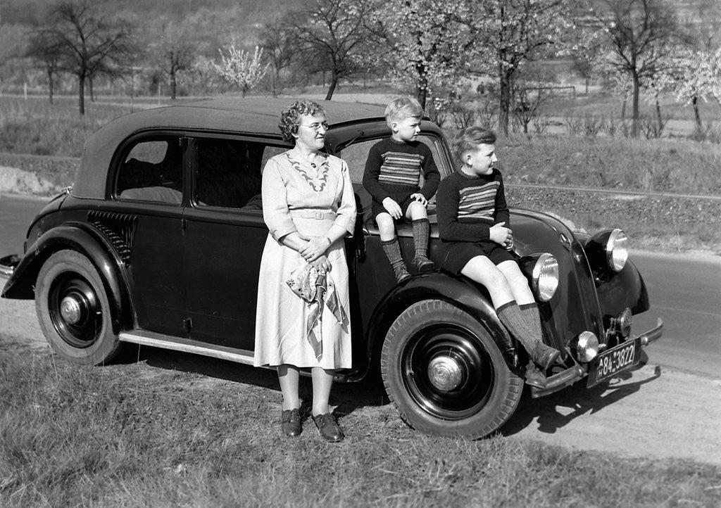 Detail of Mother stands next to her two sons sitting on the hood of their Mercedes automobile, ca. 1950 by Anonymous