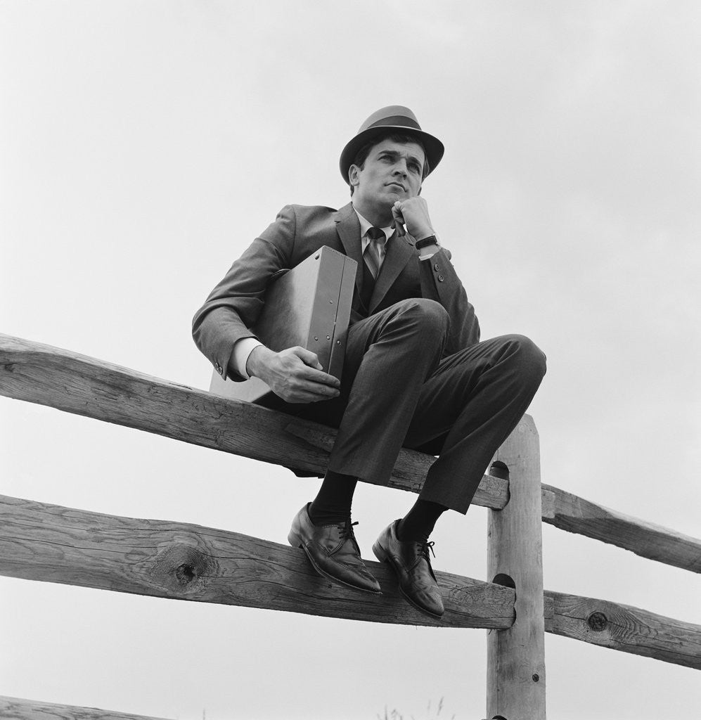 Detail of Businessman sitting on fence worried expression holding briefcase by Anonymous