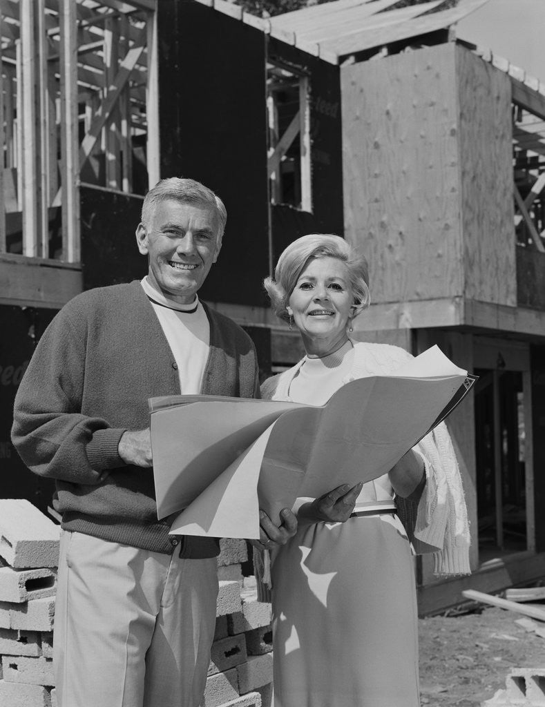 Detail of Smiling mature couple holding blueprints on home construction site by Anonymous