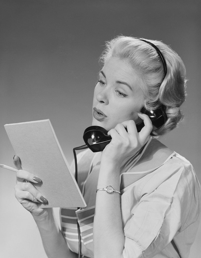 Detail of Blond woman talking on telephone reading list by Corbis