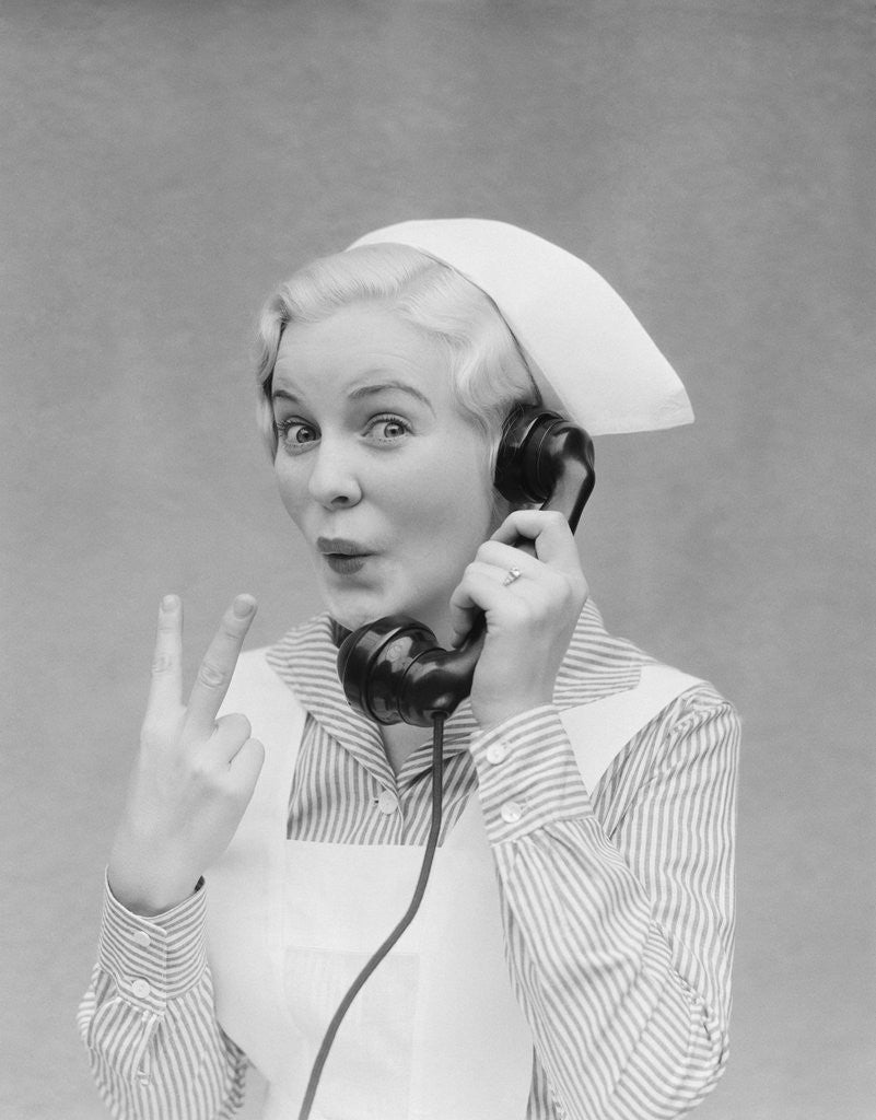 Detail of Smiling blond nurse with surprised expression talking on telephone holding up two fingers by Anonymous