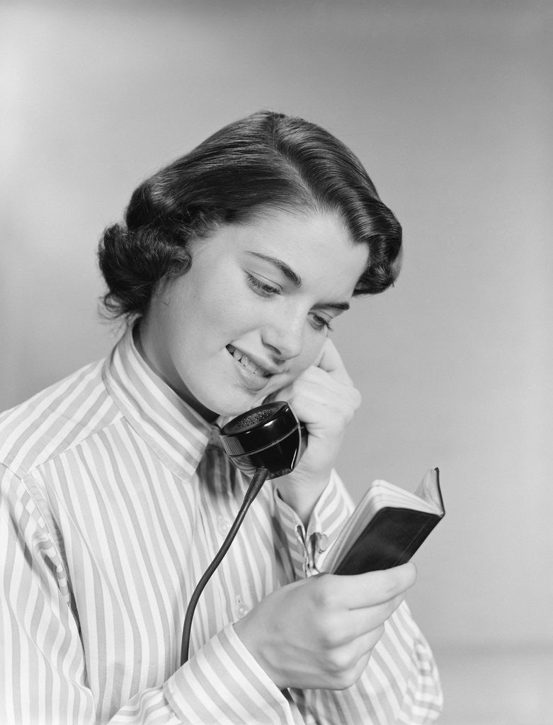 Detail of Young woman talking on telephone reading address from little black book by Anonymous