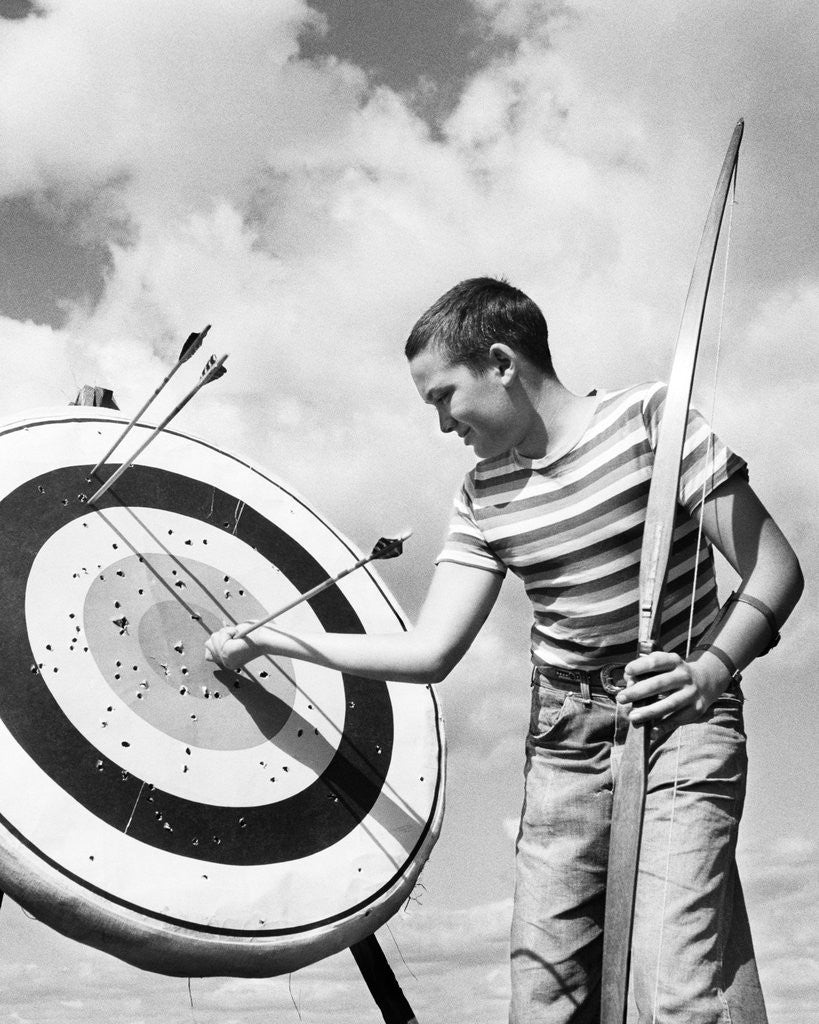 Detail of Boy jeans striped t-shirt holding bow & pulling arrow out of target bull's-eye by Anonymous