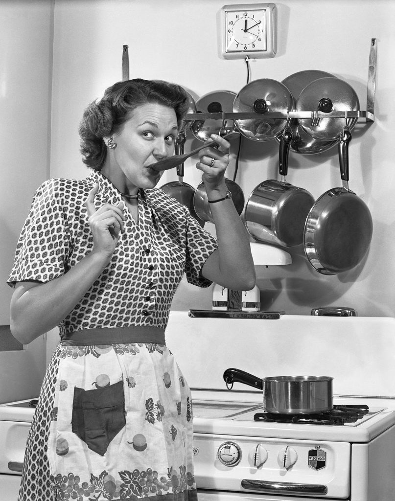 Detail of Housewife tasting with spoon by stove funny facial expression by Anonymous