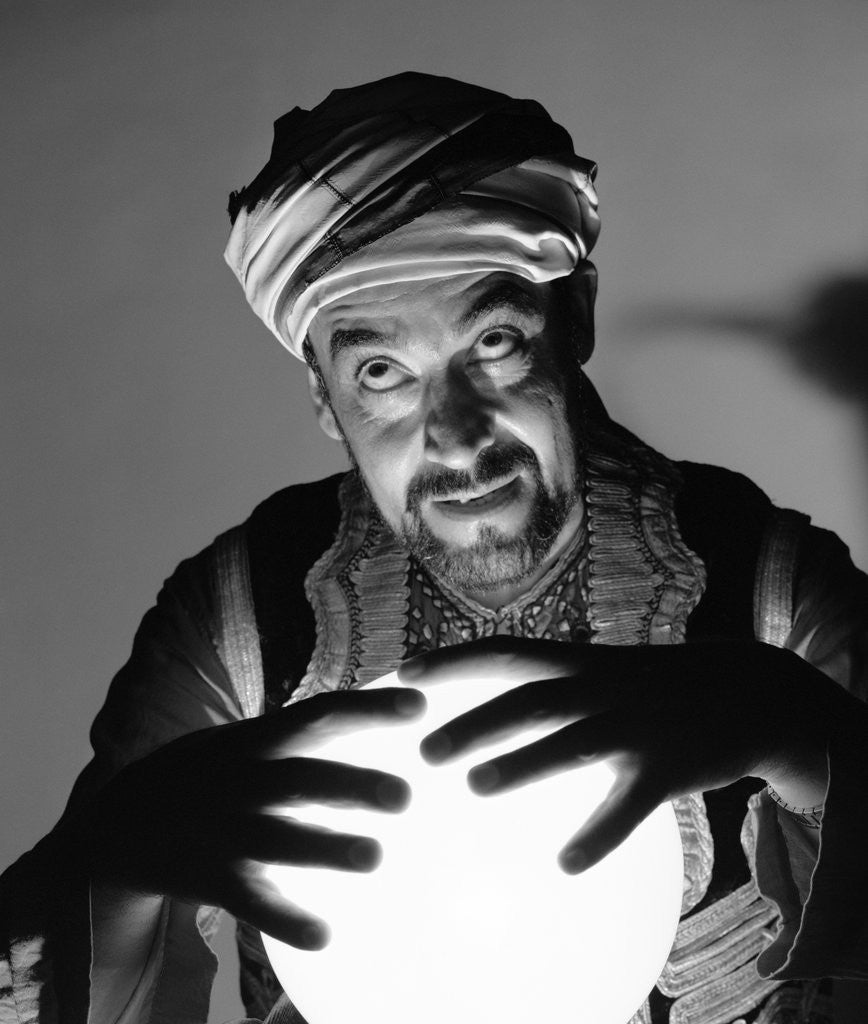 Detail of Scary fortune teller man with hands on lighted crystal ball wearing turban by Anonymous