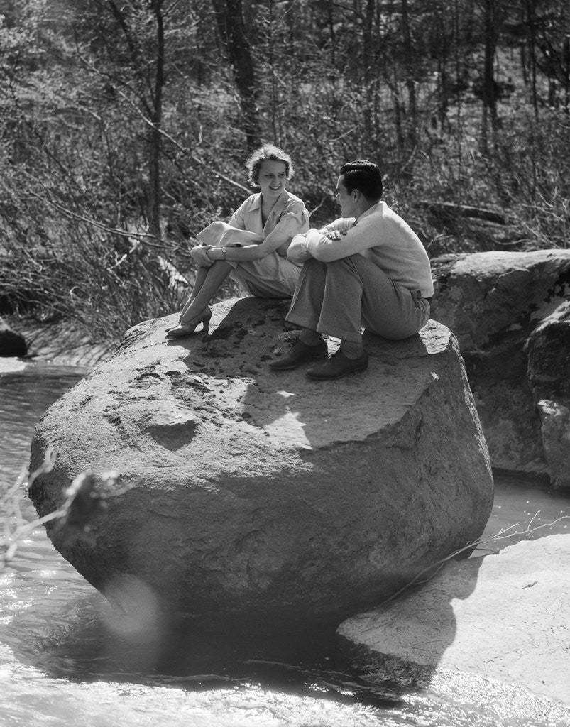 Detail of Couple man woman sitting on large rock in stream hugging knees smiling happy romance by Anonymous