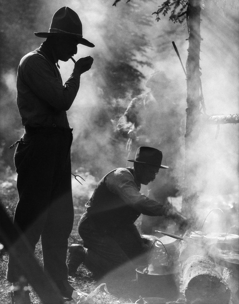 Detail of Three men cowboys camping one man smoking pipe one man cooking over campfire moody silhouette by Anonymous