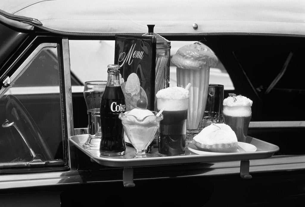 Detail of Food tray with soda fountain items on car window at 1950s style drive-in restaurant by Corbis