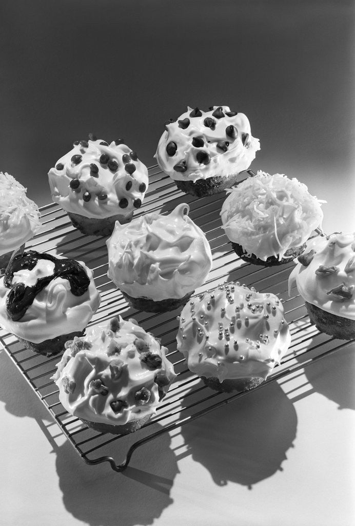 Detail of Cupcakes on metal bakers cooling rack decorated with icing sprinkles chips by Anonymous
