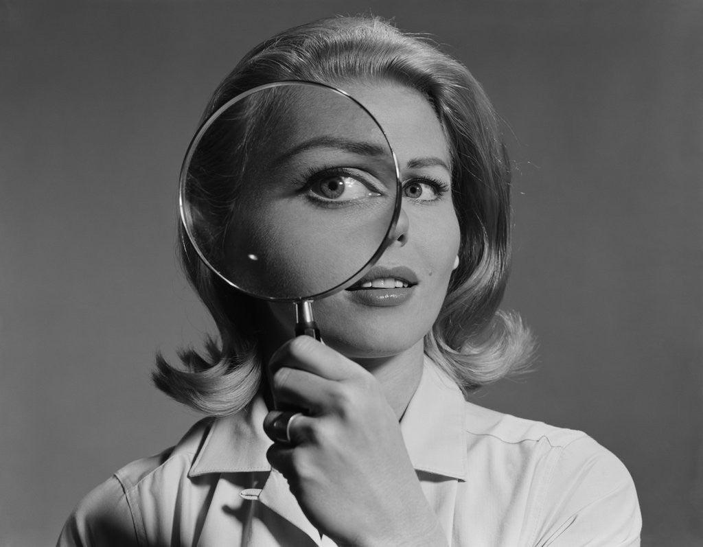 Detail of Blond woman magnifying glass held up to and enlarging one eye by Anonymous