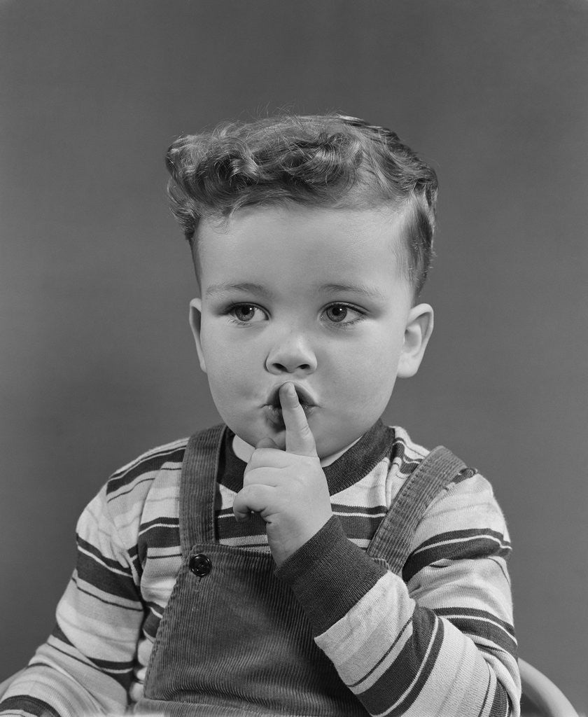 Detail of Little boy making shush shushing quiet silence sign with finger to mouth lips by Corbis