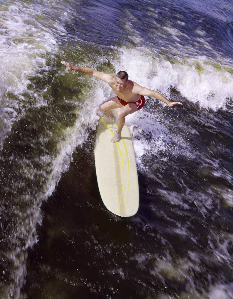 Detail of Young man red swim trunks yellow surfboard riding a wave surfing by Corbis