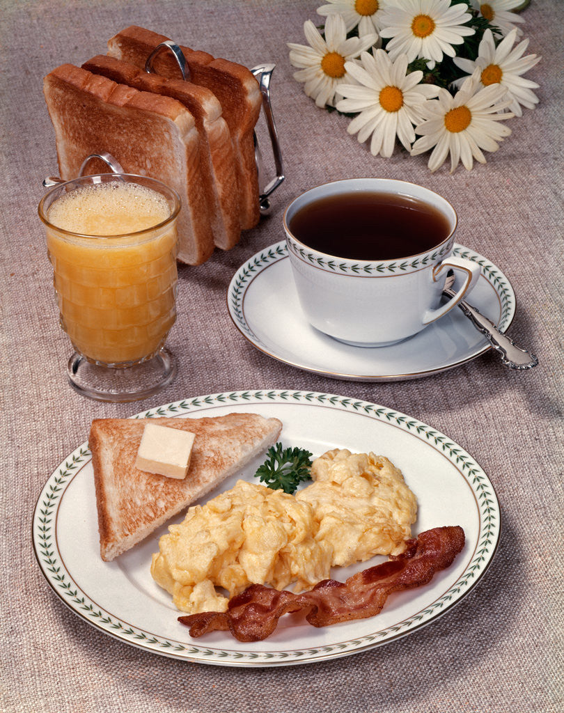 Detail of Scrambled eggs bacon toast on dish glass orange juice toast in rack cup of coffee daisies breakfast by Anonymous