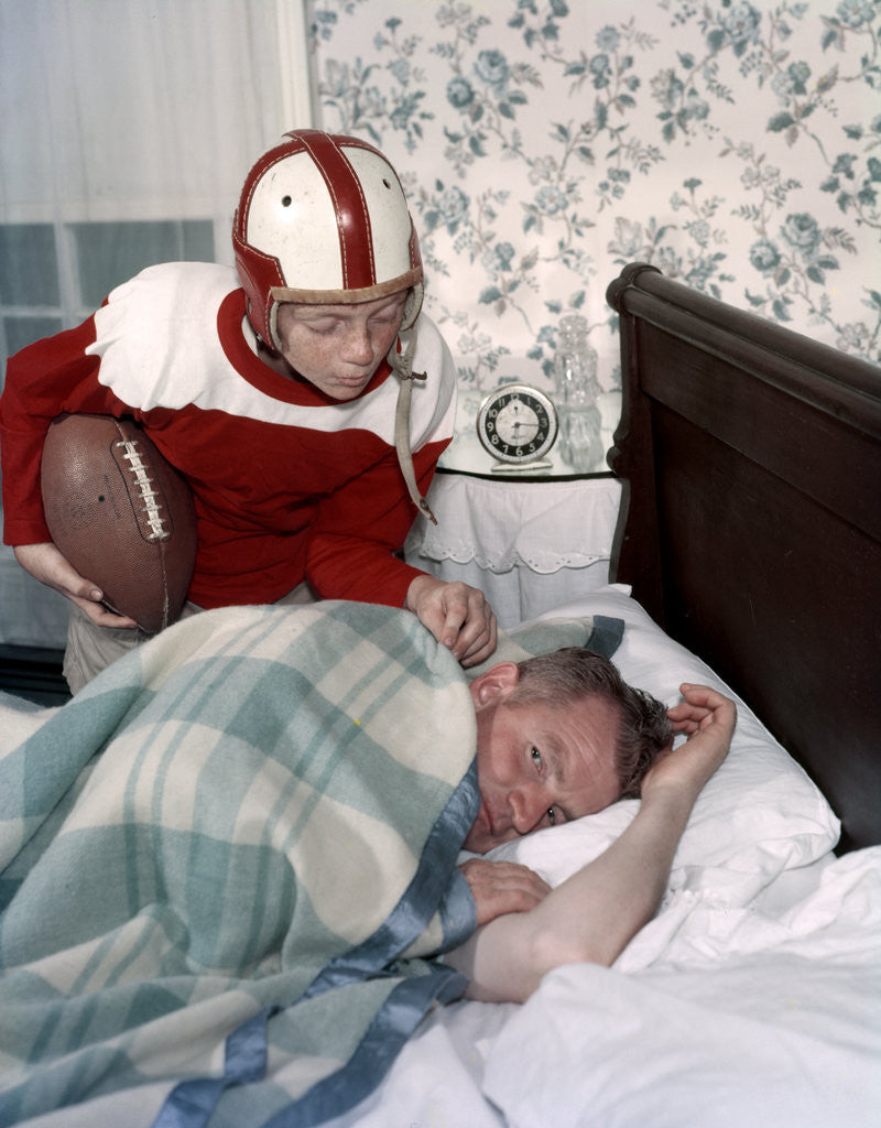 Boy in football uniform waking father asleep in bedroom by Corbis