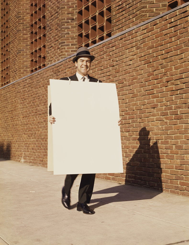 Detail of Smiling man wearing suit necktie and hat walking carrying large sandwich board by Corbis