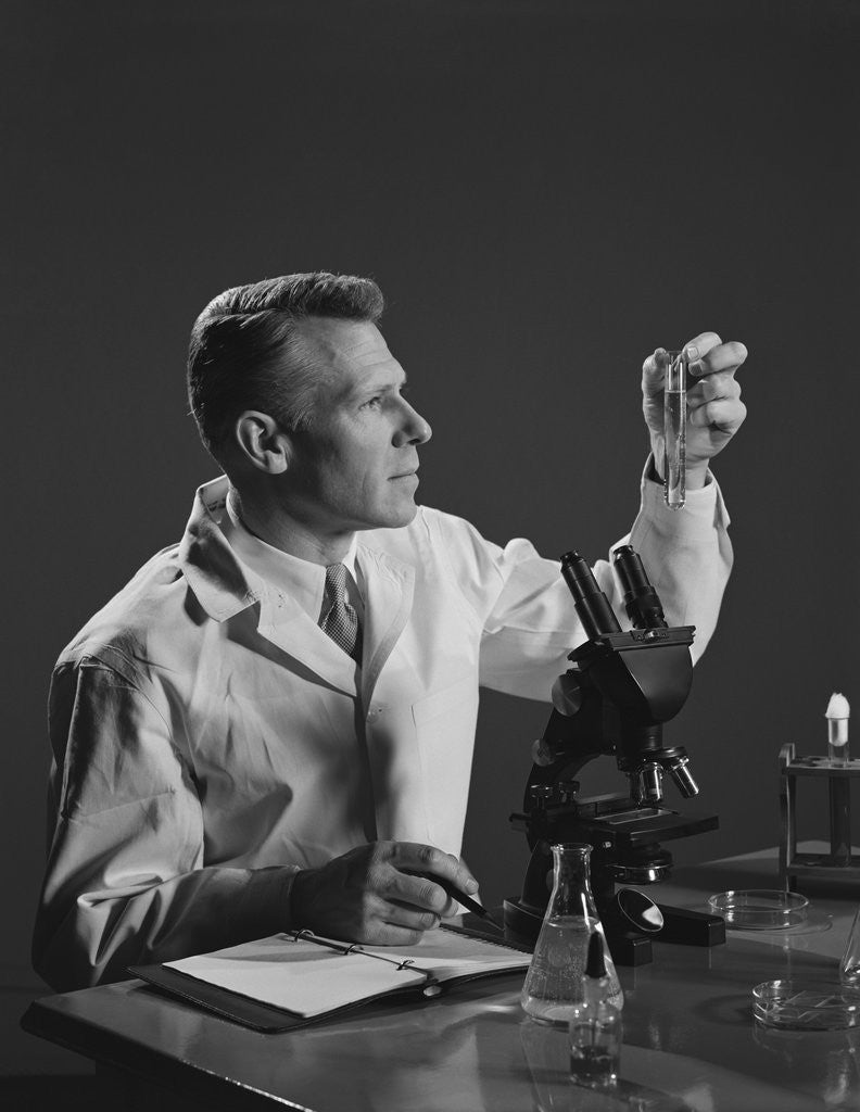 Detail of Man scientist holding test tube making notes by microscope by Anonymous