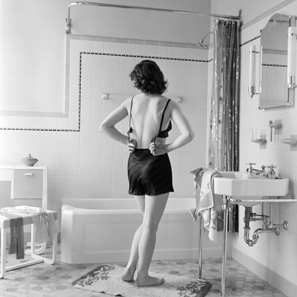Detail of Back view of woman in bathroom fastening black bra by Anonymous