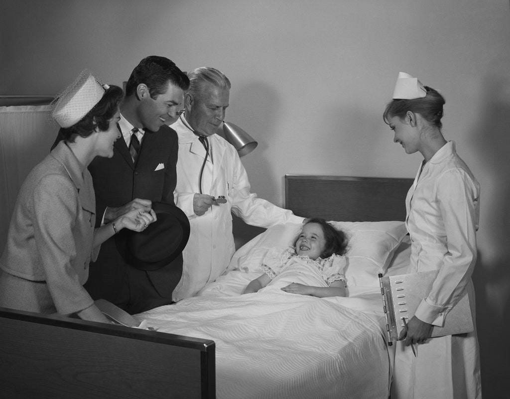 Detail of Man doctor woman nurse mother father seeing visiting smiling little girl patient in hospital bed by Corbis