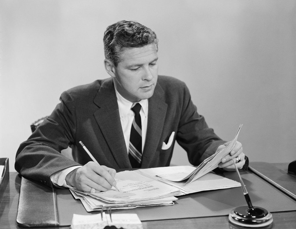 Detail of Businessman at desk looking over files papers making notes with pencil by Anonymous