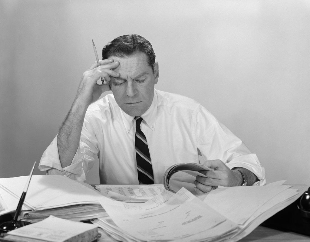 Detail of Businessman desk full papers hand to forehead serious expression by Anonymous