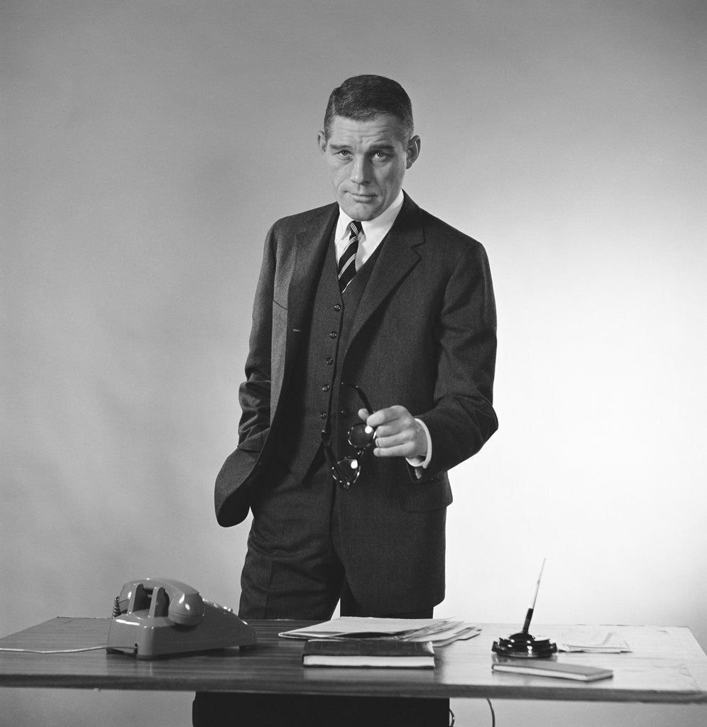 Detail of Serious businessman three piece suit standing behind desk gesturing with glasses by Corbis