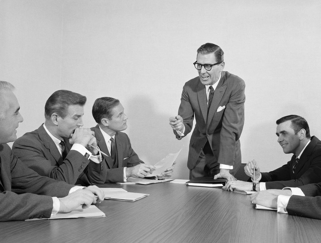 Detail of 5 executive businessmen meeting at conference table one man standing by Anonymous